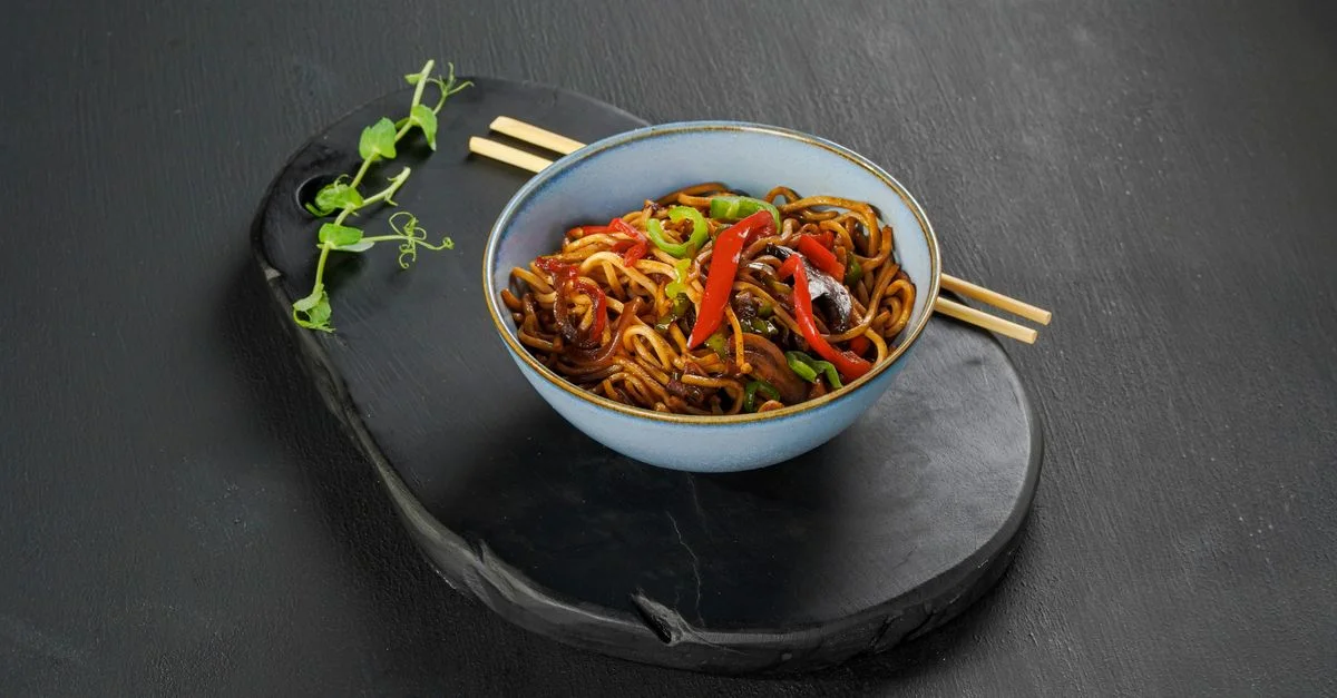 Bol coloré de nouilles aux légumes, servi sur une élégante ardoise noire.