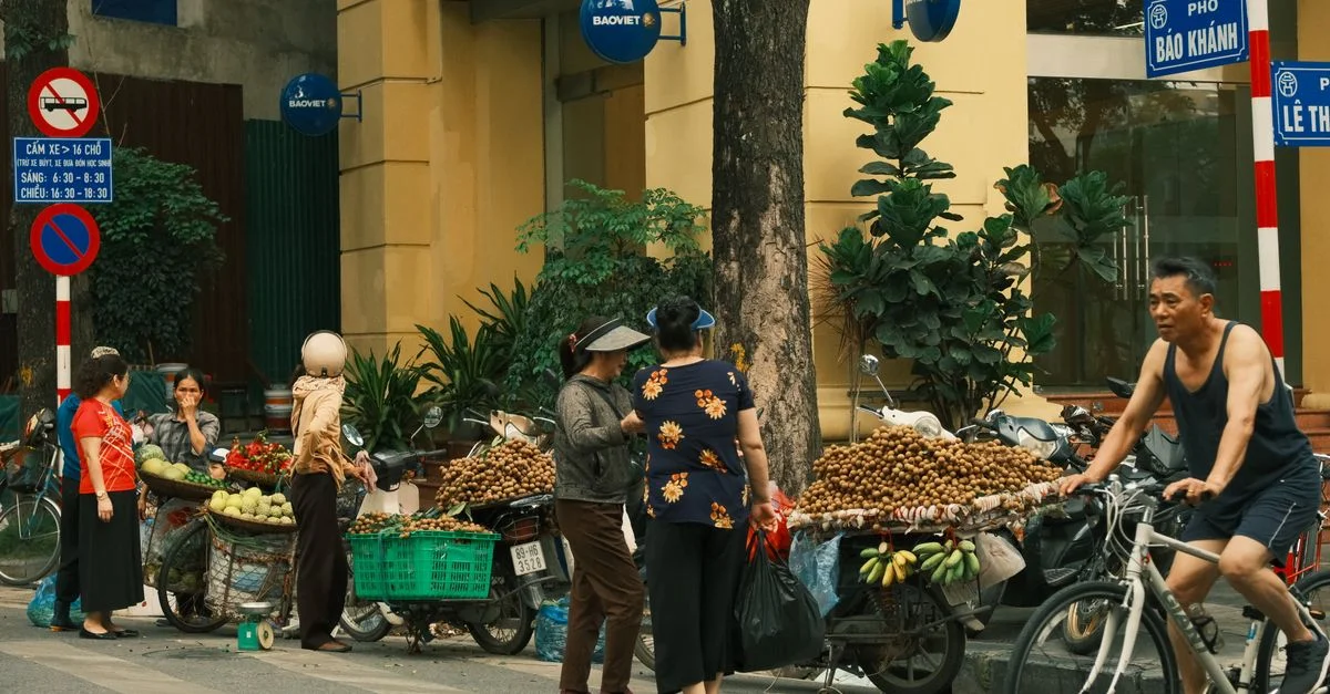 Un marché de rue animé à Hanoï avec des vendeurs vendant des fruits à vélo, mettant en valeur la culture vietnamienne locale.