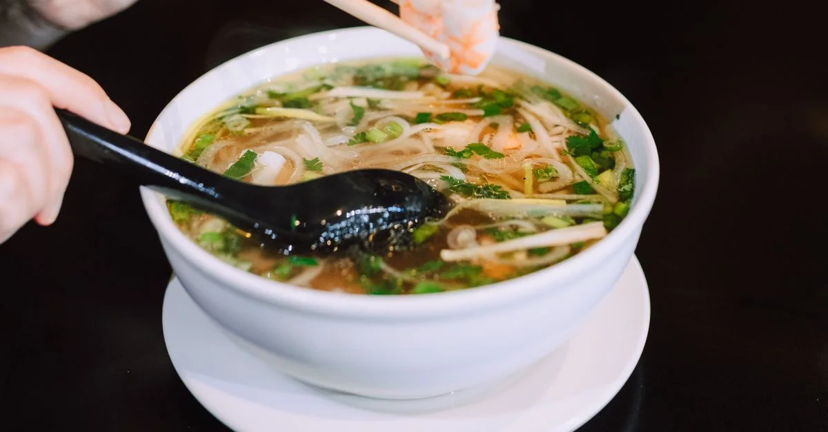 Bol délicieux de pho vietnamien avec des nouilles, des herbes et des crevettes, servi avec des baguettes.