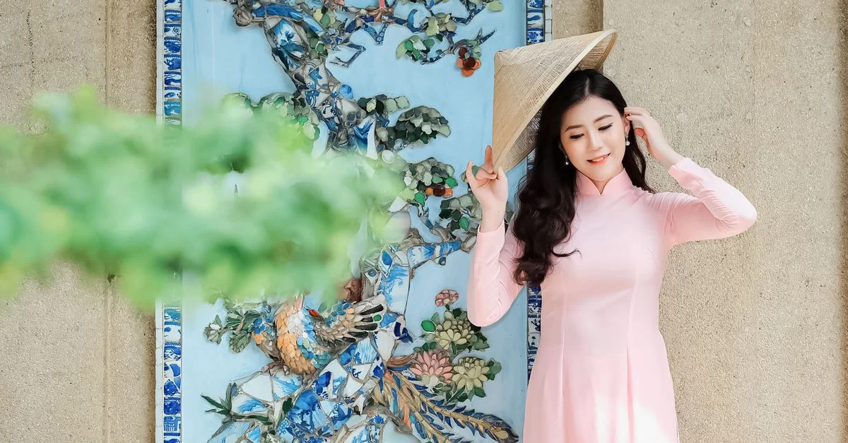 Une femme magnifique en tenue traditionnelle posant avec un chapeau contre un mur décoratif.