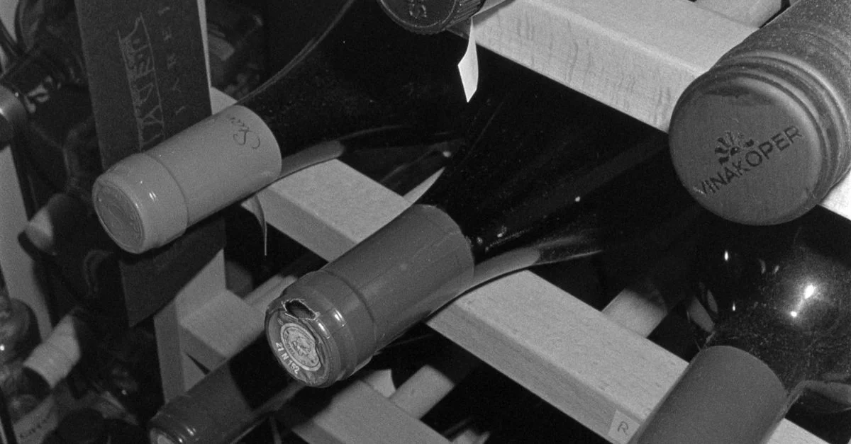 Image en monochrome de bouteilles de vin rangées sur une étagère en bois évoque une atmosphère classique et élégante.