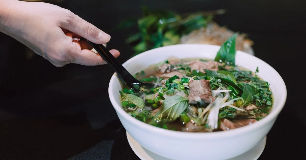 Gros plan sur une main tenant des baguettes au-dessus d'un bol de pho vietnamien savoureux.