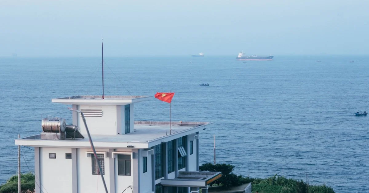Vue panoramique d'un bâtiment avec un drapeau vietnamien près de la mer de Vũng Tàu, avec des navires visibles au loin.