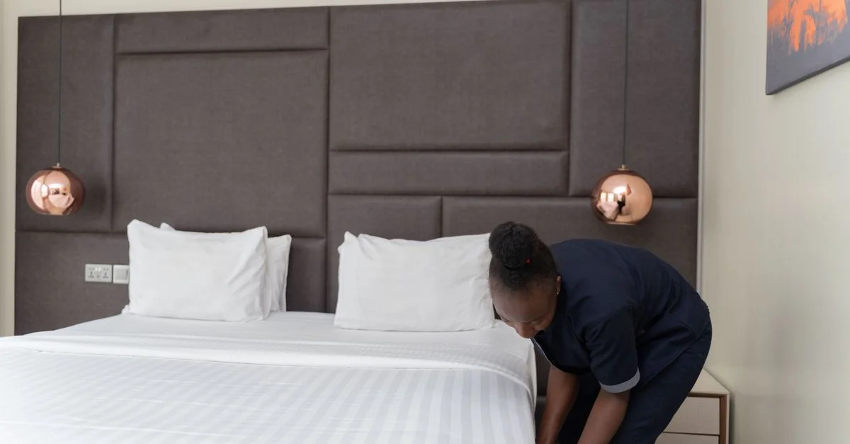 Un membre du personnel de l'hôtel prépare un lit dans une chambre d'hôtel moderne et élégante avec des accents en cuivre.