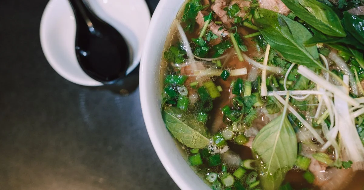 Délicieuse soupe pho vietnamienne traditionnelle avec des herbes fraîches et des garnitures dans un bol blanc.