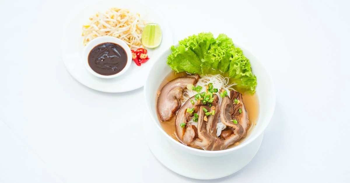 Un gros plan de soupe de nouilles au porc asiatique avec de la laitue, des garnitures et un plat d'accompagnement.