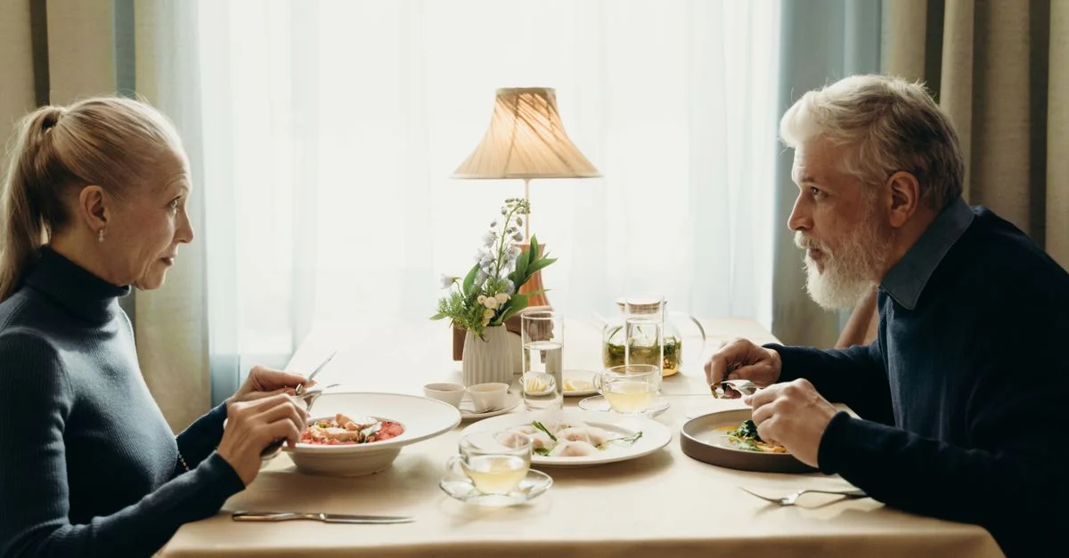 Un couple âgé profitant d'un repas ensemble dans un cadre intérieur chaleureux et éclairé.