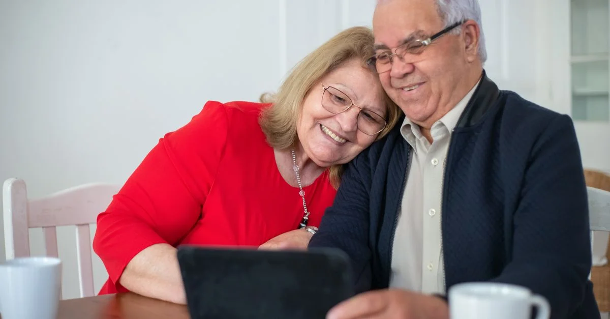 Couple âgé souriant utilisant une tablette ensemble dans un cadre intérieur confortable.