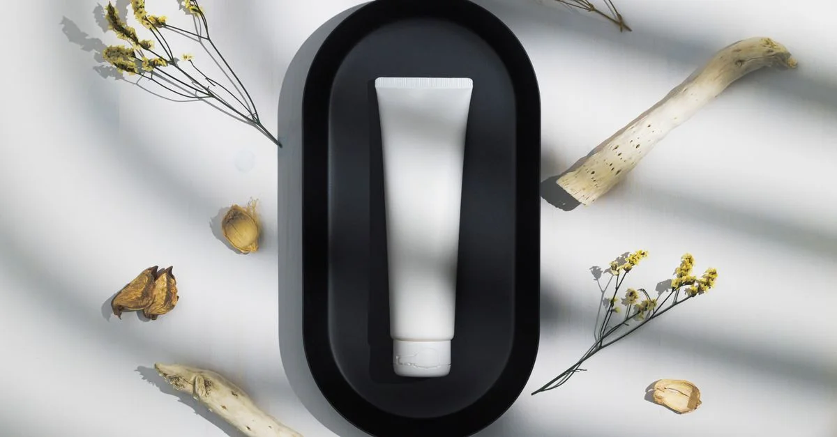 Élégant tube de soins de la peau sur un plateau noir entouré d'éléments naturels séchés sous des ombres douces.