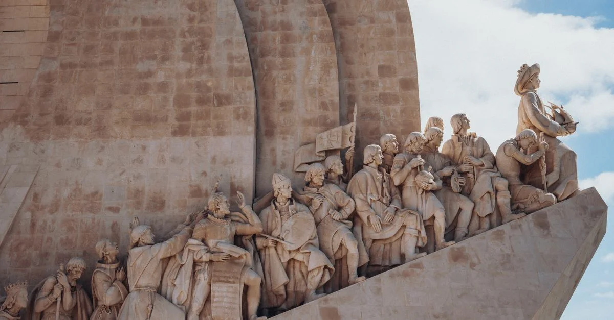 Gros plan sur le Monument des Découvertes à Lisbonne, mettant en valeur des figures historiques en détail sculpté sous un ciel dégagé.