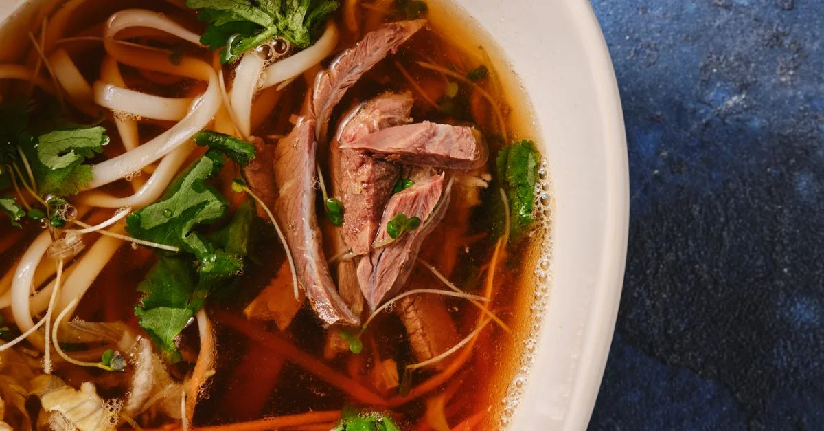 Délicieuse soupe de nouilles au bœuf asiatique garnie d'herbes fraîches, capturée en gros plan sur un fond bleu.