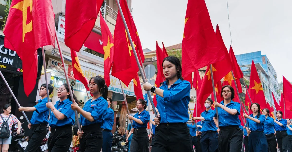 Défilé animé de jeunes adultes brandissant des drapeaux rouges dans une rue de Hô Chi Minh-Ville.