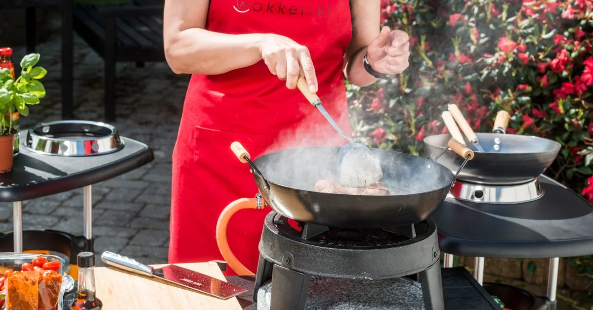 Une personne cuisine dans un wok en plein air, mettant en valeur des ingrédients frais et un style de cuisson vibrant.