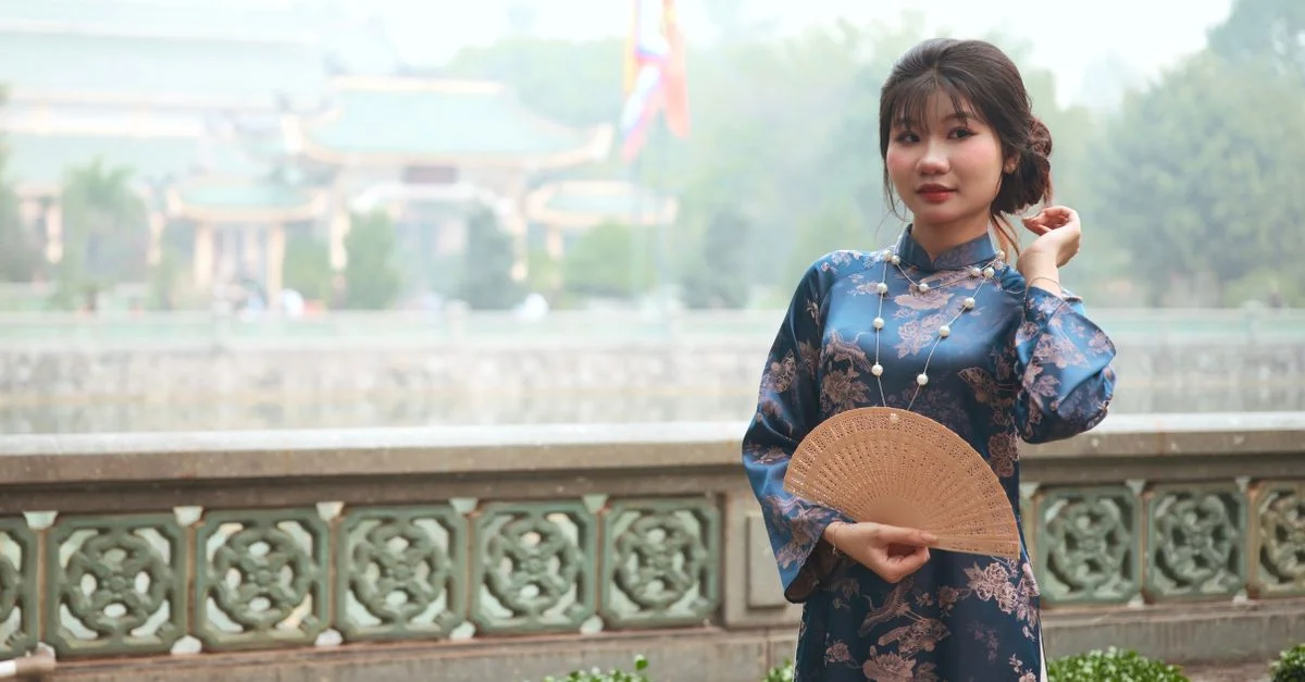 Jeune femme en tenue traditionnelle tenant un éventail en plein air, mettant en valeur la beauté culturelle.